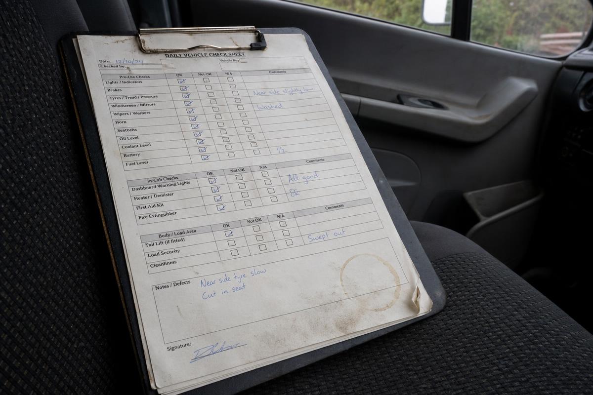 A worn paper vehicle check sheet with biro marks on a van seat